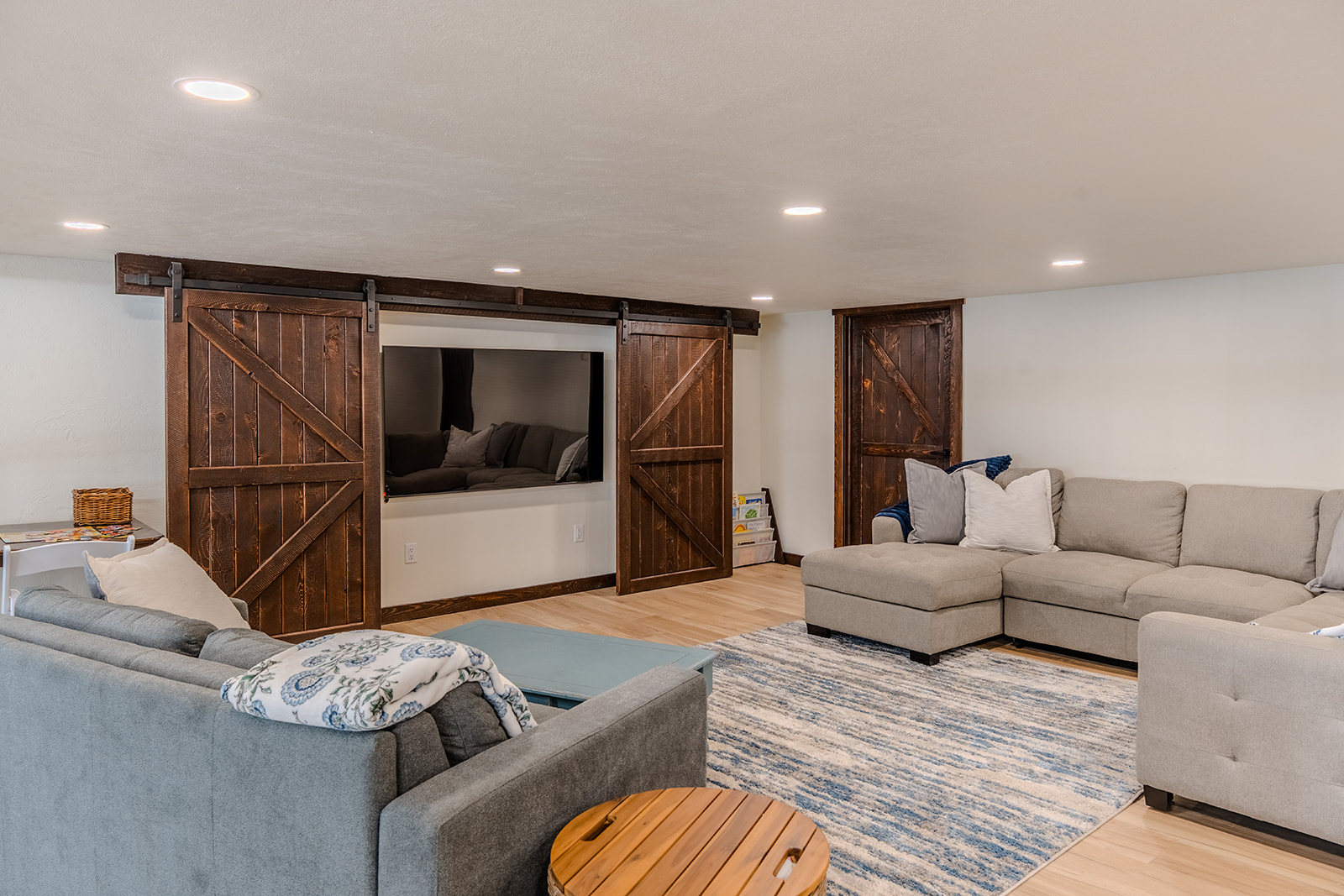 Well-lit basement living room with custom barn doors and sectional seating